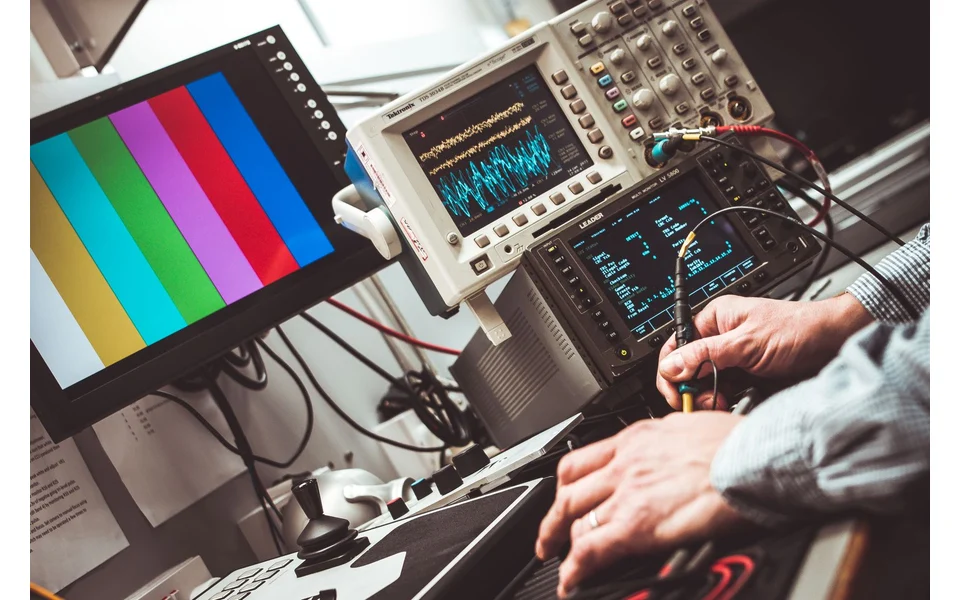 An engineer taking measurements at an electronic test bench with a connected oscilloscope displaying signal traces.